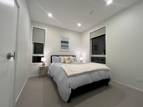 a white bedroom with a bed and two windows at Stunning executive family home! in Paraparaumu