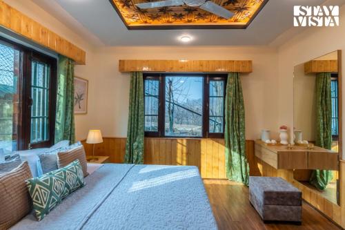 a bedroom with a bed and a desk and windows at StayVista at Riverscape with Views, WiFi, Heater in Srinagar