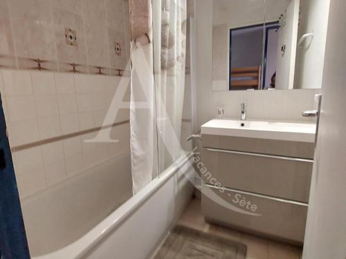 une salle de bain avec un lavabo, une baignoire et un miroir dans l'établissement Studio cabine en rez de jardin dans residence avec piscine, à Sète
