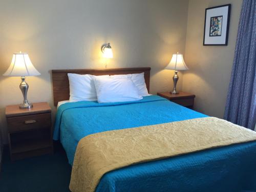 a hotel room with a bed with blue sheets and two lamps at East Street Inn & Suites in Tipton