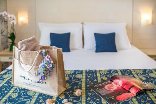 a bed with a book and a bag on it at Hotel San Giorgio Resort 4S in Caorle