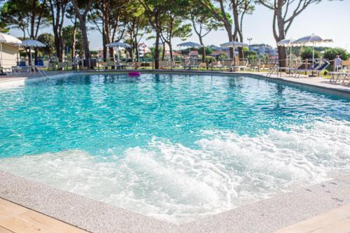 a swimming pool with blue water and chairs and umbrellas at Hotel San Giorgio Resort 4S in Caorle