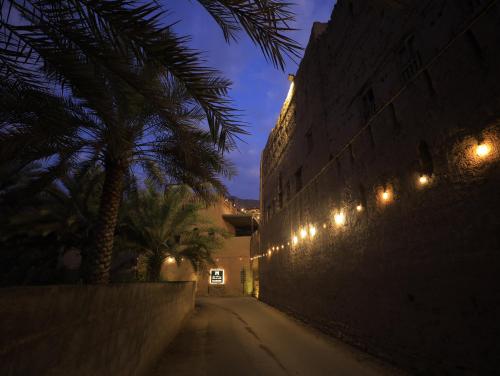 an empty street at night with lights on a wall at بيت الصباح نزل وكافيه Bait AlSabah Heritage Inn & Cafe in Birkat al Mawz