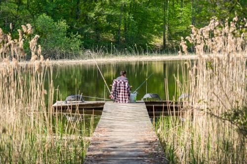 a person standing on a dock fishing on a lake at Ośrodek Wypoczynkowy Camping Tumiany in Tumiany