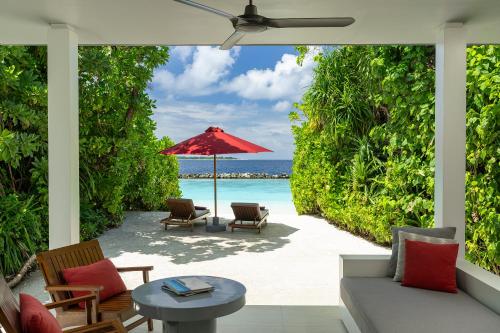 a patio with chairs and an umbrella and the ocean at Dhigali Maldives - A Premium All-Inclusive Resort in Raa Atoll