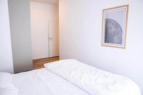 a white bed in a white room with a picture on the wall at Rigeli Apartments in Kosovo Polje