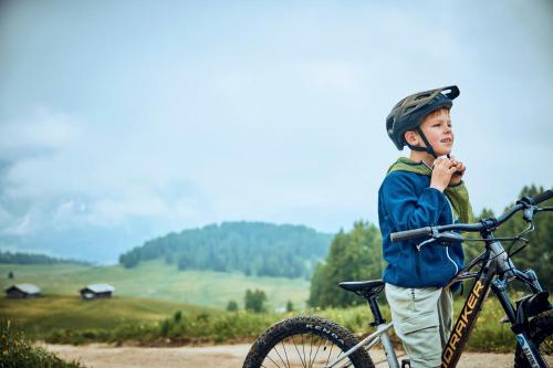 a young boy wearing a helmet standing next to a bike at COMO Alpina Dolomites in Alpe di Siusi