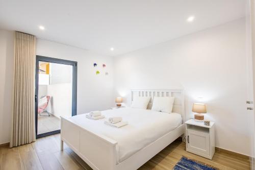 a white bedroom with a large white bed and a window at Baia Mar T1 - By Smarthomes in São Martinho do Porto