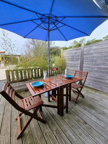 a wooden table with two chairs and a blue umbrella at Résidence de Nodeven in Guissény