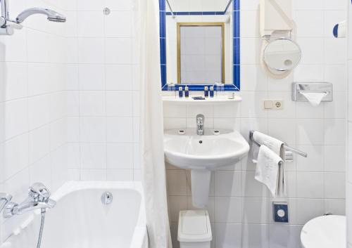 a white bathroom with a sink and a tub and a toilet at Grand Hotel Cravat in Luxembourg