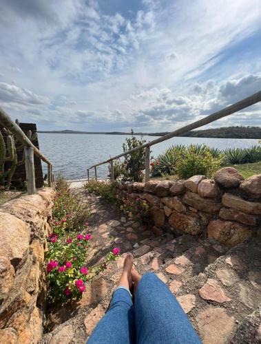a person sitting on a rock wall next to the water at Hotel Fazenda Monte Cristo in Piranhas