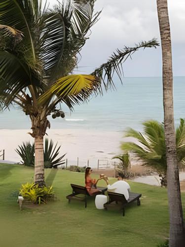 two people sitting on benches in front of the beach at Vila Corada in Pipa
