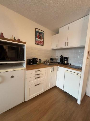 une petite cuisine avec des armoires blanches et un micro-ondes dans l'établissement APPARTEMENT RESIDENCE PLEIN SUD , CENTRE STATION , PIED DES PISTES , PARKING ,WIFI , 30 m2 , 4p, à Les Deux Alpes