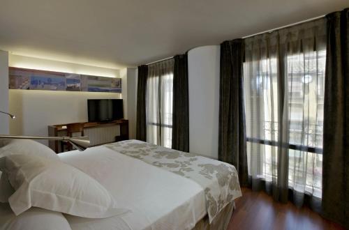 a bedroom with a white bed and large windows at Hotel Sancho Abarca Petit SPA in Huesca