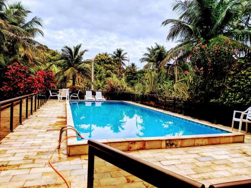 a swimming pool in a resort with chairs and palm trees at Chácara Morada do Sol in Sepetiba