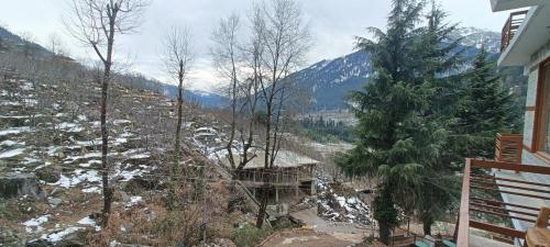 a view of a snowy mountain with a house and trees at Hotel Nayra in Manāli