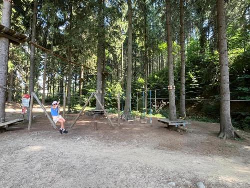 a woman sitting on a swing in a park at Apartmán Resident A001 - BEZBARIÉROVÝ Apartmán ideální pro rodiny s dětmi, v těsné blízkosti Anenského údolí, bobové dráhy, Ski areálů, Ski školy, FREE PARKING, FREE WIFI, výhled do zahrady s posezením na terase, dětské hřiště v areálu in Harrachov