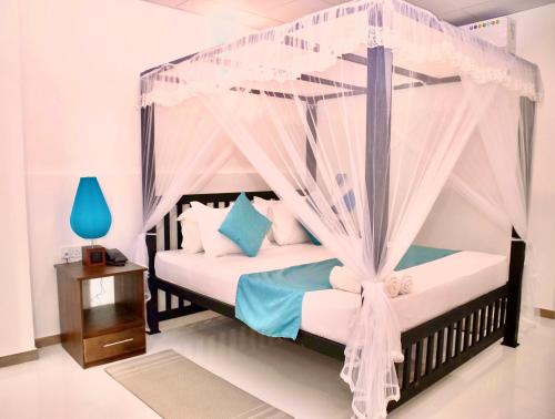 a bedroom with a canopy bed with white sheets and blue pillows at Alnaro Hotel & Resort in Moratuwa
