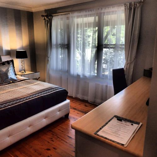 a bedroom with a bed and a desk and a window at Bowral Road Art Gallery Bed and Breakfast in Mittagong