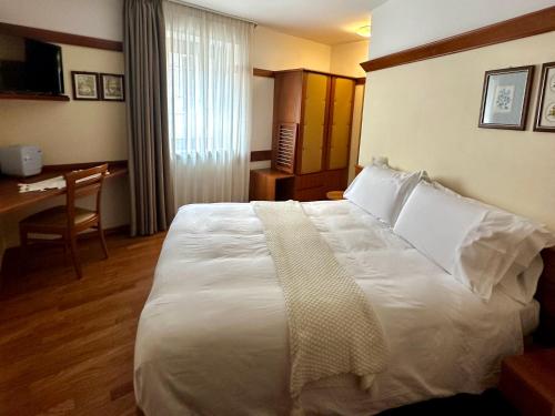 a hotel room with a large white bed and a desk at Il Duca Degli Abruzzi in Pescasseroli