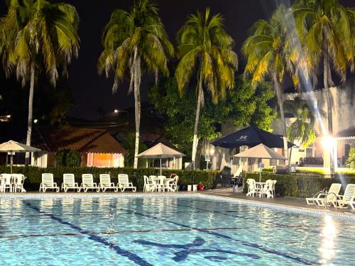 a swimming pool with chairs and palm trees at night at Hotel Los Puentes Comfacundi in Girardot