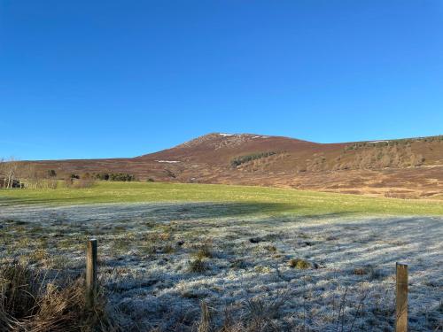 a dirt road in a field with a hill in the background at Falls Cottage in Glenlivet