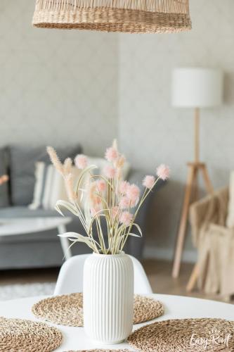 a white vase with pink flowers on a table at Pinea 110 - basen, sauna, jacuzzi w cenie pobytu - bezpośredni widok na morze - Easy - Rent Apartments in Pobierowo