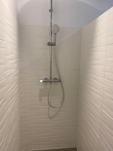 a shower with a hose in a white tiled bathroom at Charmante maison du XVIII en pierre rénovée in Colleville-Montgomery