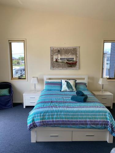 a bedroom with a bed with a colorful comforter and two windows at Seaview on The Esplanade in Portarlington