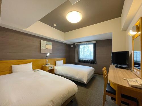 a hotel room with two beds and a desk and a television at Hotel Route-Inn Yokote Inter in Yokote