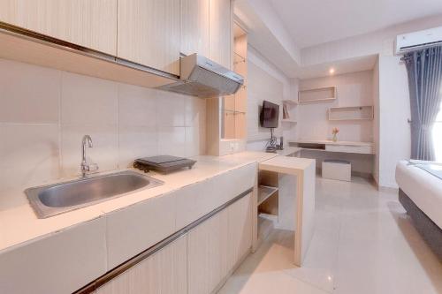 a white kitchen with a sink and a couch at Cozy Living Studio at Paramount Skyline Apartment By Travelio in Tangerang