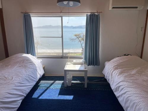 a bedroom with two beds and a window with the ocean at Megijima Island Guesthouse & cafe Megino in Takamatsu