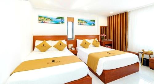 a bedroom with two beds with white sheets and yellow pillows at Mira Eco Hotel Quy Nhon in Quy Nhon