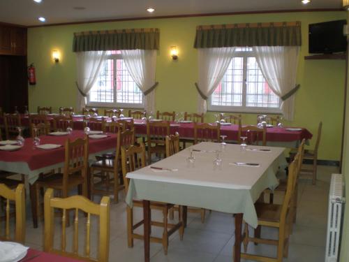 uma sala de jantar com mesas, cadeiras e janelas em Hostal Catro Ventos em Lugo