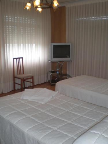 a bedroom with two beds and a tv and a chair at Hostal Catro Ventos in Lugo