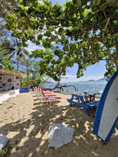 a group of picnic tables and a surfboard on the beach at Secret Garden Family House in Ko Chang