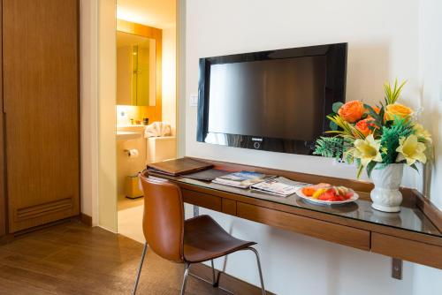 a room with a desk with a television and a vase of flowers at On 8 Sukhumvit Nana Bangkok by Compass Hospitality in Bangkok
