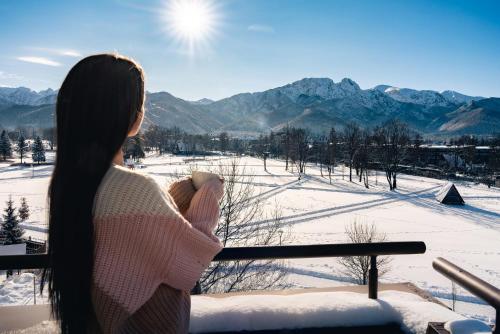 a woman standing on a balcony looking at the snow covered mountains at Hotel Helios 300m od Krupówek nowy BASEN od 12 lipca in Zakopane