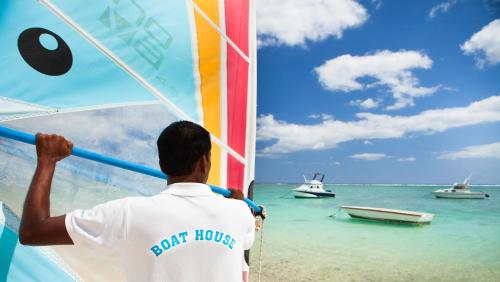 a man standing on the beach looking at boats in the water at Pearle Beach Resort & Spa in Flic-en-Flac