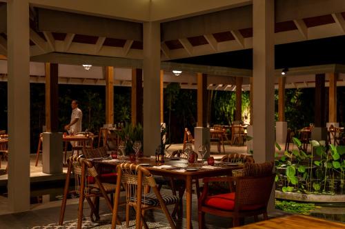 a restaurant with tables and chairs with a woman walking in the background at Dhigali Maldives - A Premium All-Inclusive Resort in Raa Atoll