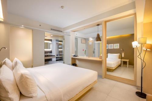 a bedroom with a large white bed and a bathroom at Sevn Legian in Legian