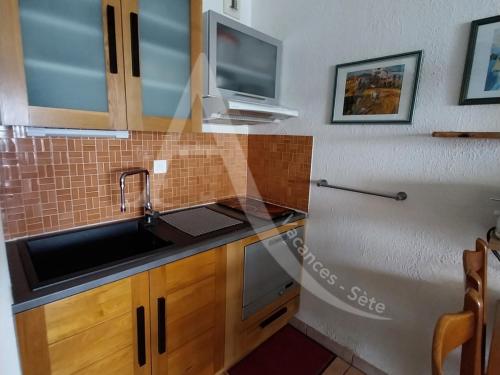 Il comprend une cuisine avec un évier et une télévision murale. dans l'établissement CONFORTABLE T2 EN FRONT DE MER, PARKING, WI-FI, à Sète