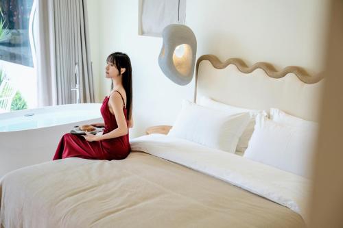 a woman in a red dress sitting on a bed at 礼橖LoveTime·美学海景民宿（较场尾大鹏所城店） in Shenzhen