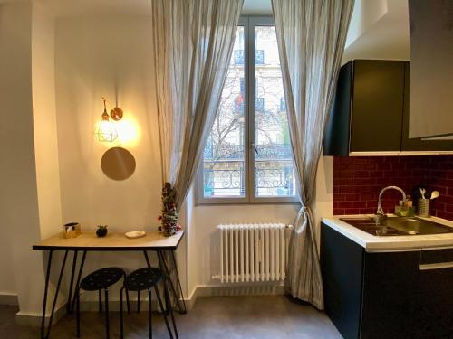 une cuisine avec une table et deux tabourets devant une fenêtre dans l'établissement Charmant 2 pièces au coeur de Paris, à Paris