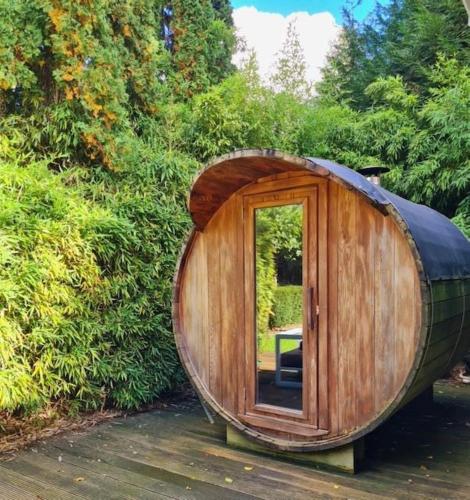 a large wooden barrel with a door in a garden at Cozy tiny house with swimming pool & outdoor sauna in Waasmunster