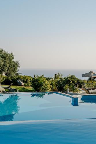 a large blue swimming pool with the ocean in the background at Village Heights Resort in Hersonissos