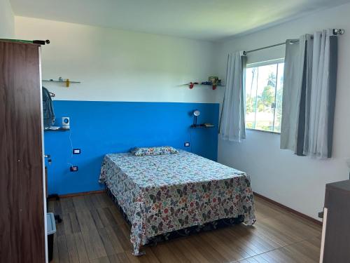 a bedroom with a bed with blue walls and a window at Casa Itacimirim in Camacari