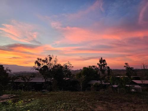 a sunset over a field with trees and buildings at Black Sheep House Khaoyai by ALPHATEL PARTNER in Pong Talong