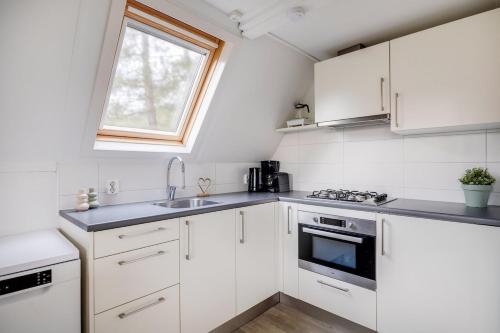 a kitchen with white cabinets and a sink and a window at Rietzanger I Cottage met Mooie Inrichting in Zwiggelte