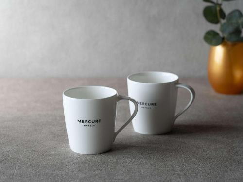 two white coffee mugs sitting next to each other at Mercure Kochi Tosa Resort & Spa in Geisei